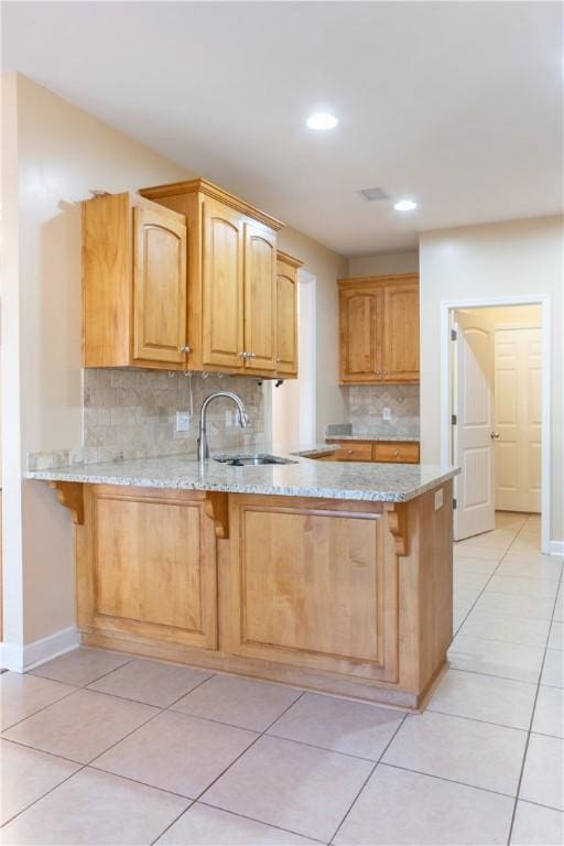 kitchen with kitchen peninsula, light stone countertops, sink, and decorative backsplash