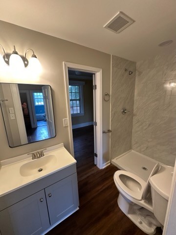 bathroom featuring hardwood / wood-style floors, vanity, toilet, and a tile shower