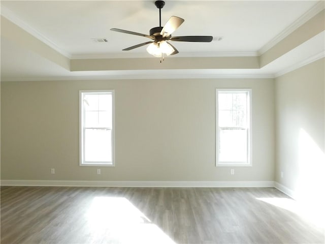 empty room with ceiling fan, a raised ceiling, wood-type flooring, and ornamental molding