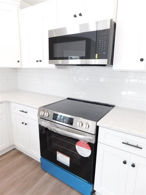 kitchen featuring white cabinets, tasteful backsplash, appliances with stainless steel finishes, and light hardwood / wood-style flooring