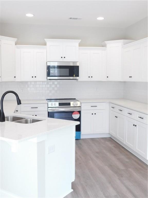 kitchen with sink, stainless steel appliances, tasteful backsplash, light hardwood / wood-style flooring, and white cabinets