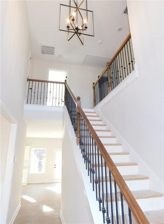 staircase with hardwood / wood-style flooring, an inviting chandelier, and a high ceiling