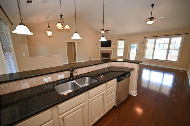 kitchen featuring a tile fireplace, sink, stainless steel dishwasher, dark stone counters, and pendant lighting