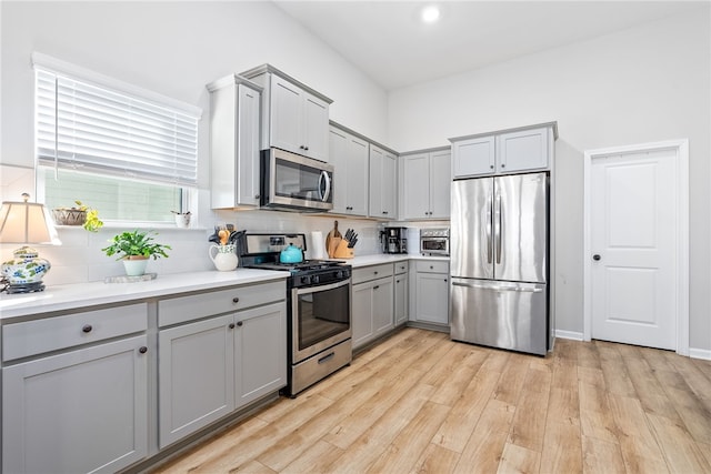 kitchen featuring light hardwood / wood-style floors, backsplash, appliances with stainless steel finishes, and gray cabinetry