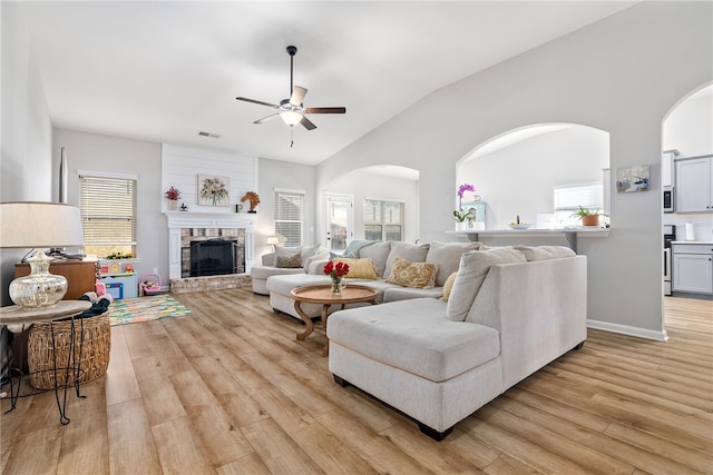 living room featuring light wood-type flooring, vaulted ceiling, a brick fireplace, and ceiling fan