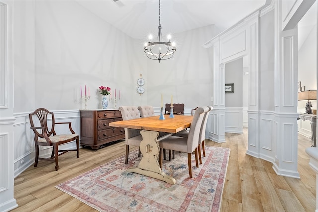 dining room with light wood-type flooring, a chandelier, and ornate columns