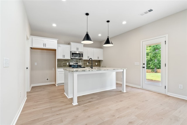 750 Mcdonald Dr, Opelika, AL 36801 - kitchen featuring appliances with stainless steel finishes, white cabinets, backsplash, light wood-style floors, and an island with sink