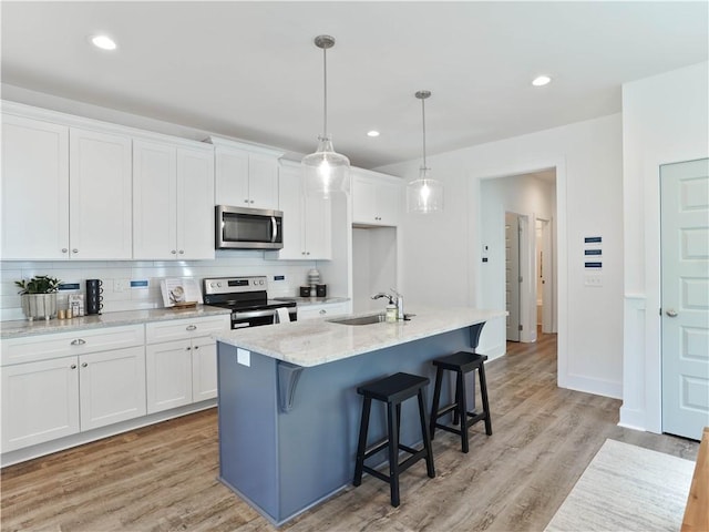 kitchen featuring appliances with stainless steel finishes, white cabinetry, an island with sink, decorative backsplash, and hanging light fixtures