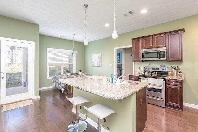 kitchen featuring stainless steel appliances, visible vents, hanging light fixtures, a kitchen island with sink, and a sink