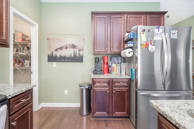 kitchen with light stone counters, dark wood-type flooring, baseboards, dark brown cabinets, and freestanding refrigerator