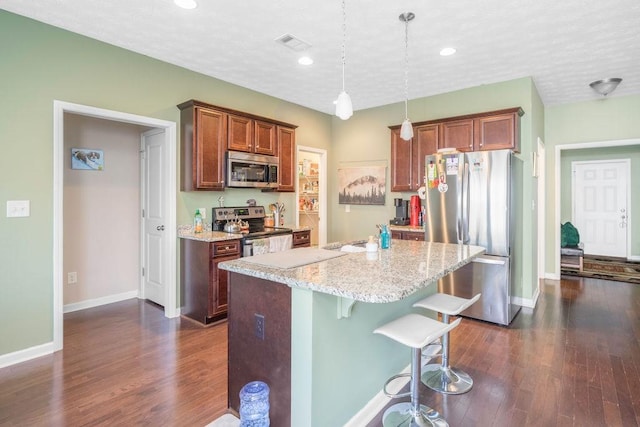 kitchen featuring a breakfast bar area, visible vents, appliances with stainless steel finishes, an island with sink, and decorative light fixtures