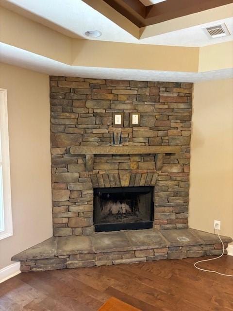 interior details with a stone fireplace, wood finished floors, visible vents, and baseboards