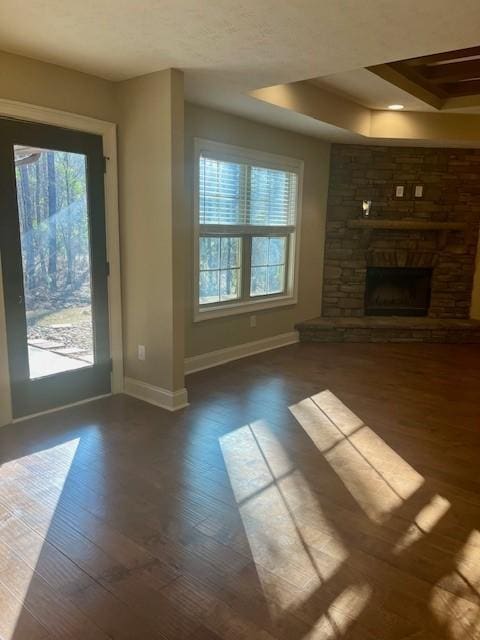 unfurnished living room with a tray ceiling, baseboards, wood finished floors, and a stone fireplace