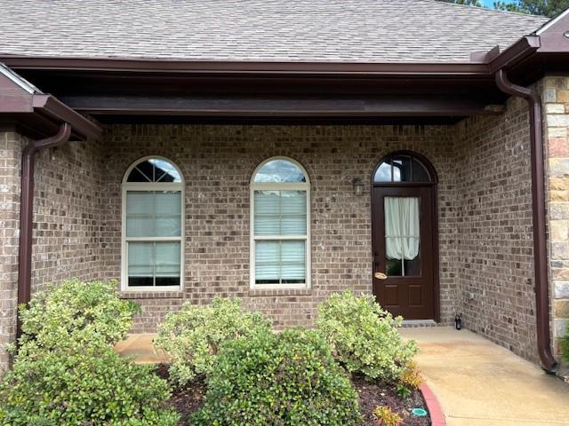 doorway to property featuring a shingled roof and brick siding