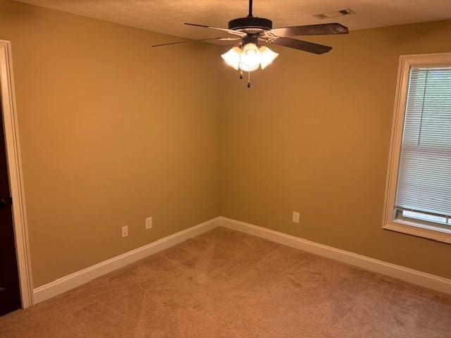 unfurnished room featuring baseboards, visible vents, a ceiling fan, light colored carpet, and a healthy amount of sunlight