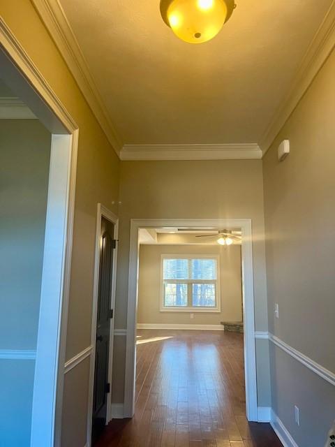 hall featuring dark wood finished floors, crown molding, and baseboards