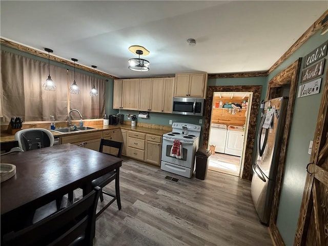 kitchen with washing machine and clothes dryer, stainless steel appliances, a sink, light brown cabinets, and wood finished floors