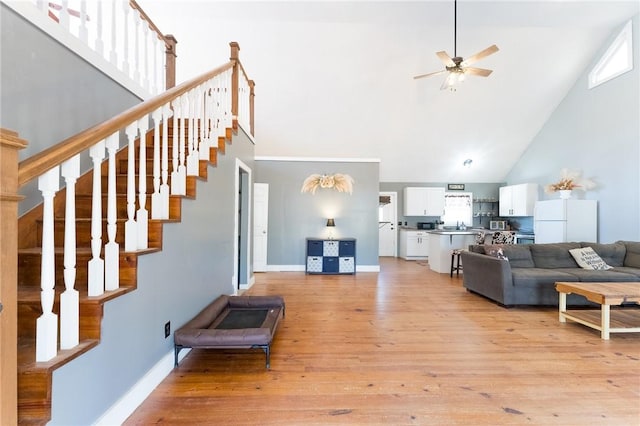 living room with a high ceiling, ceiling fan, and light wood-type flooring