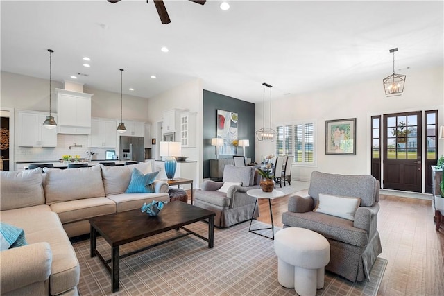 living room featuring ceiling fan with notable chandelier and light wood-type flooring