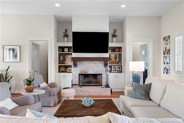 living room featuring built in shelves, light hardwood / wood-style floors, and a brick fireplace