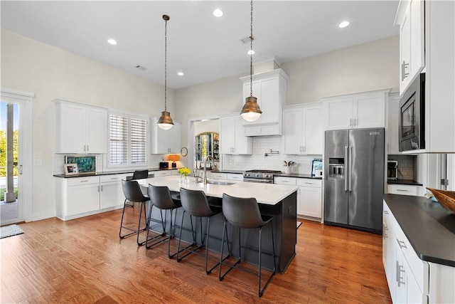 kitchen featuring white cabinetry, stainless steel appliances, a kitchen breakfast bar, an island with sink, and decorative light fixtures