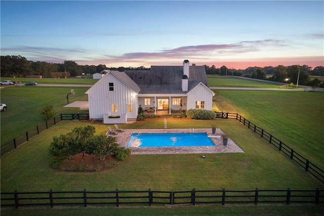 pool at dusk featuring a rural view, a yard, and a patio