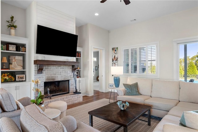 living room with hardwood / wood-style flooring, built in shelves, ceiling fan, and a brick fireplace