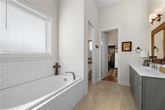 bathroom featuring tiled tub, tile patterned flooring, vanity, and toilet