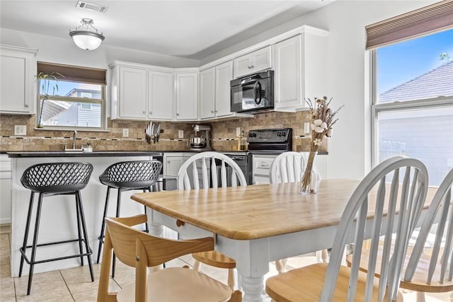 kitchen featuring tasteful backsplash, visible vents, dark countertops, light tile patterned floors, and black appliances