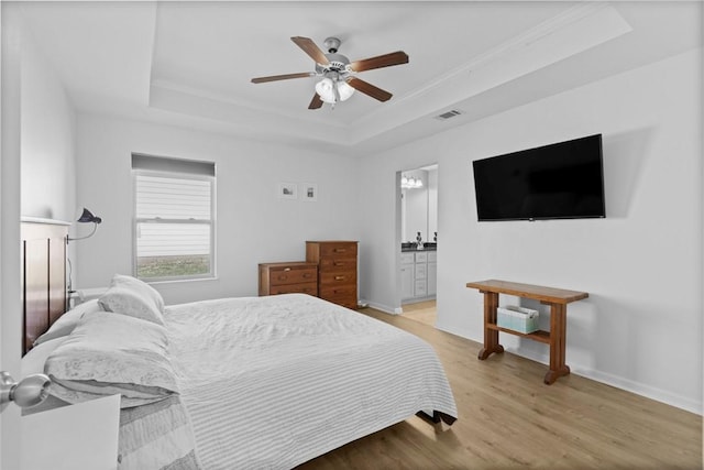 bedroom with visible vents, a tray ceiling, ensuite bath, light wood-style floors, and baseboards