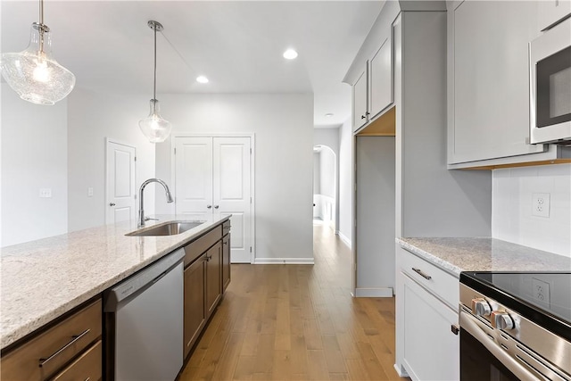 kitchen featuring light stone countertops, stainless steel appliances, light hardwood / wood-style floors, sink, and hanging light fixtures