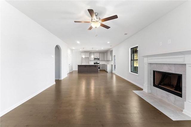 unfurnished living room with ceiling fan, dark wood-type flooring, and a tiled fireplace