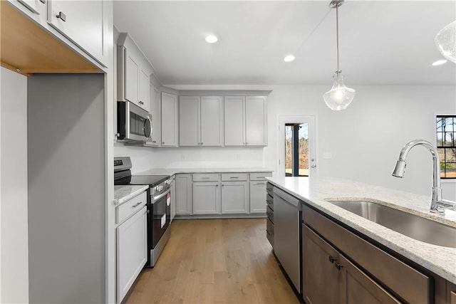 kitchen featuring appliances with stainless steel finishes, light hardwood / wood-style floors, sink, hanging light fixtures, and light stone counters