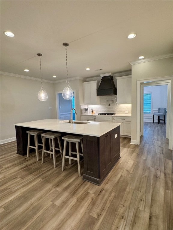 kitchen featuring premium range hood, white cabinets, sink, light hardwood / wood-style flooring, and a large island