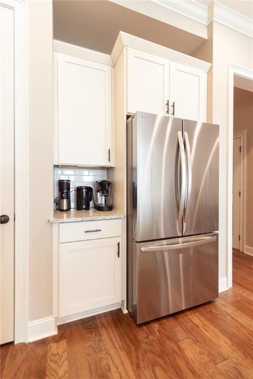 kitchen featuring stainless steel fridge, light wood-type flooring, white cabinetry, and backsplash