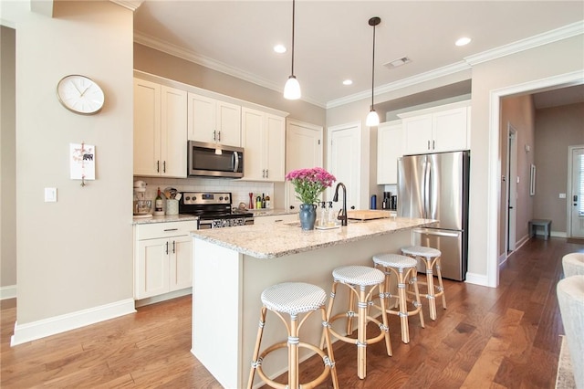 kitchen with backsplash, a kitchen island with sink, light stone counters, white cabinetry, and stainless steel appliances