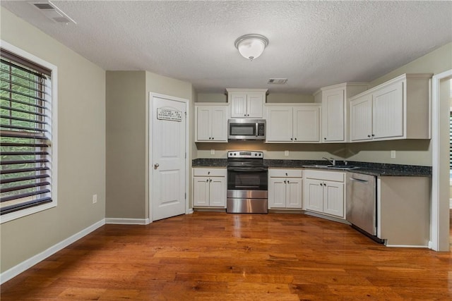 kitchen with sink, stainless steel appliances, a textured ceiling, white cabinets, and dark hardwood / wood-style flooring