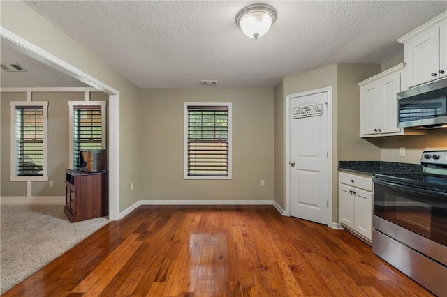 kitchen featuring stainless steel appliances, hardwood / wood-style floors, white cabinets, and a textured ceiling