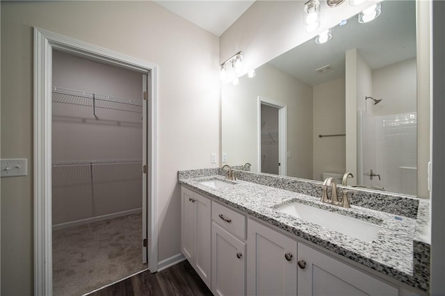 bathroom with a tile shower, double vanity, toilet, and a sink