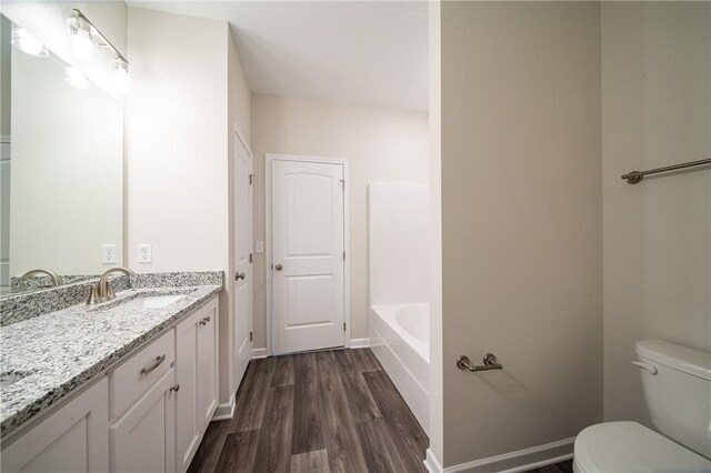 bathroom featuring a tub, baseboards, toilet, wood finished floors, and vanity