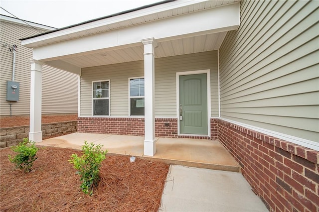 doorway to property with a porch and brick siding