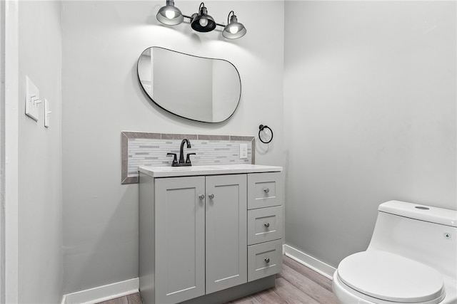 bathroom featuring toilet, wood finished floors, vanity, baseboards, and tasteful backsplash