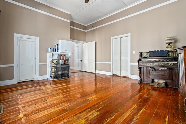 interior space with a wood stove, baseboards, ornamental molding, and wood finished floors