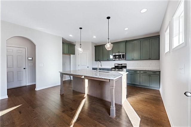 kitchen featuring a kitchen island with sink, hanging light fixtures, light stone countertops, appliances with stainless steel finishes, and tasteful backsplash