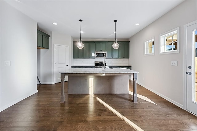 kitchen featuring a kitchen island with sink, decorative backsplash, light stone countertops, decorative light fixtures, and stainless steel appliances