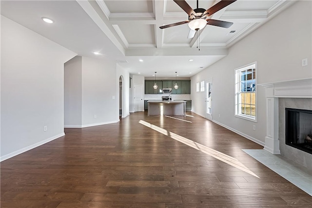 unfurnished living room featuring a tile fireplace, coffered ceiling, dark hardwood / wood-style floors, ceiling fan, and beamed ceiling