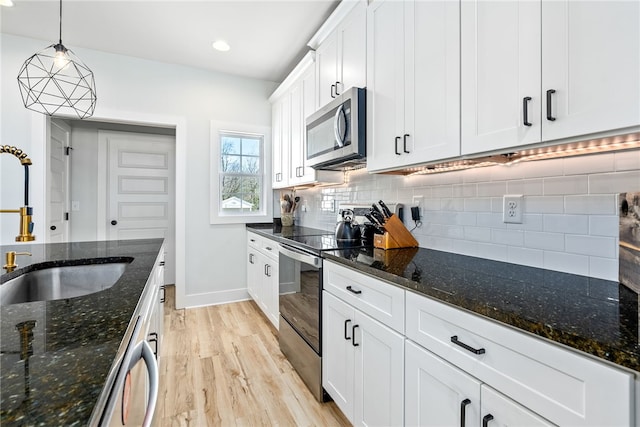 kitchen featuring tasteful backsplash, stainless steel appliances, light wood-style floors, white cabinetry, and a sink