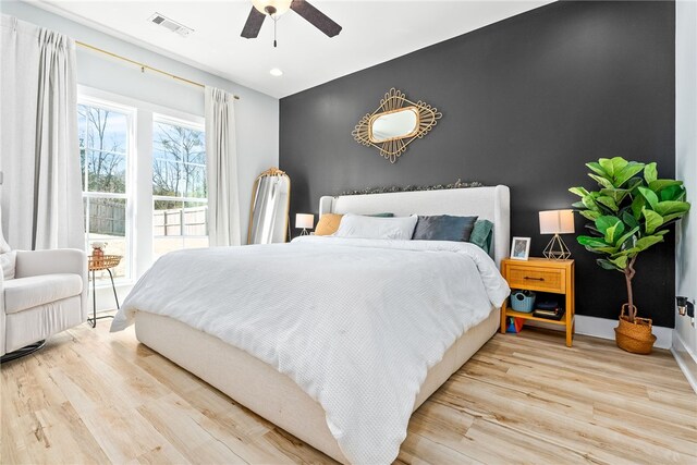 bedroom featuring visible vents, an accent wall, ceiling fan, baseboards, and wood finished floors