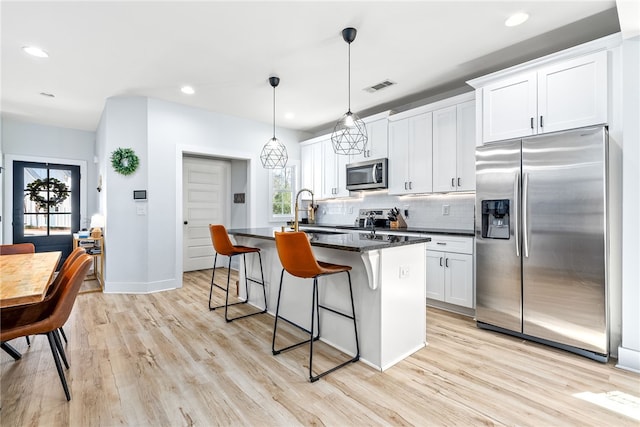 kitchen featuring visible vents, a breakfast bar, a center island with sink, a sink, and appliances with stainless steel finishes