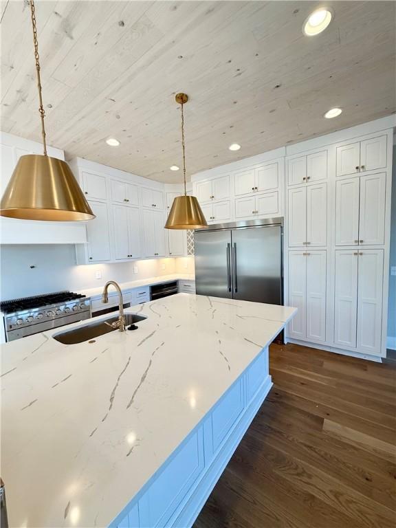 kitchen featuring sink, white cabinets, hanging light fixtures, high end appliances, and light stone countertops